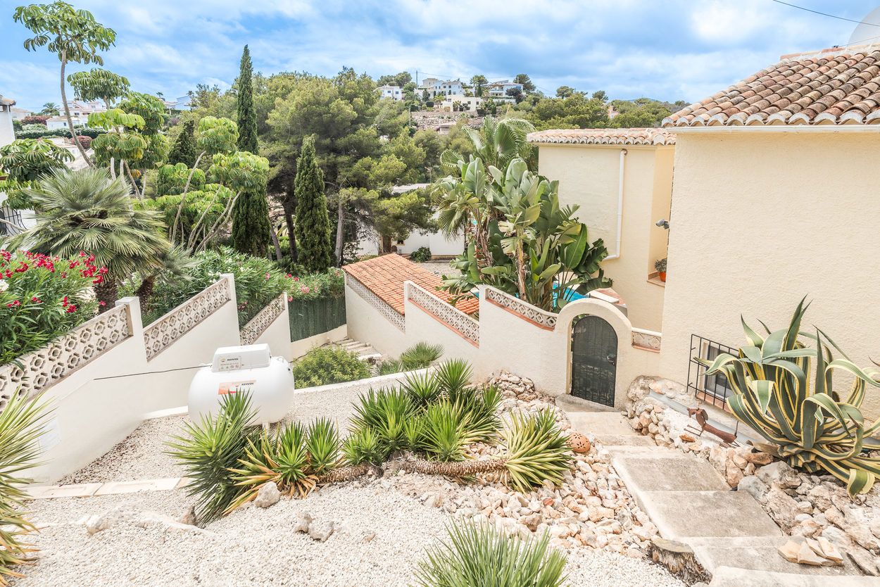Terrassierter mediterraner Garten mit weißem Kies, Yuccas und Agaven. Betonstufen führen zu einem Rundbogeneingang mit schmiedeeisernem Tor und Ziegeldächern.