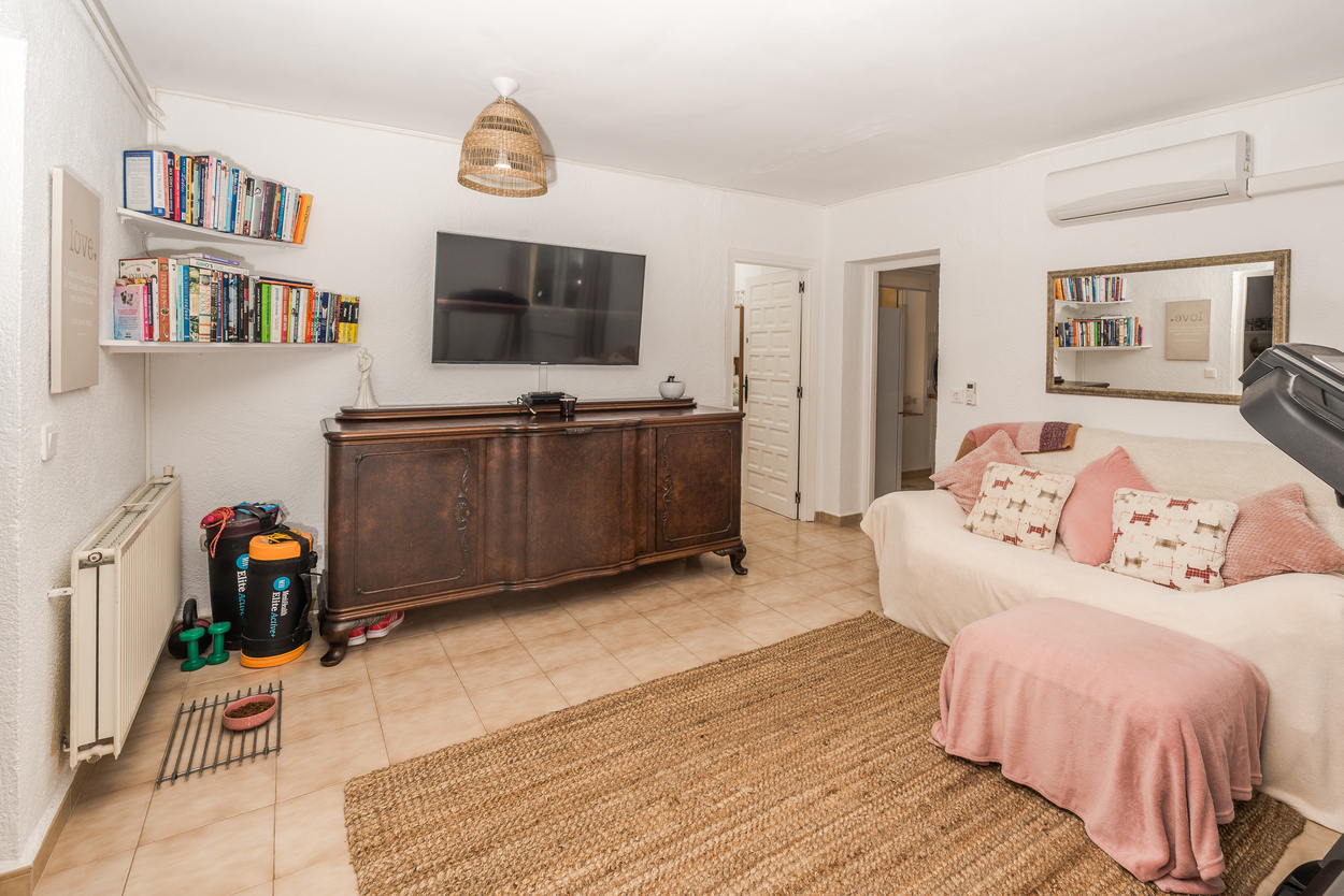 Wohnbereich mit großem Holz-Sideboard, Wand-TV und Fliesenboden. Ausgestattet mit Gas-Zentralheizung, Klimaanlage und einem Naturfaserteppich.