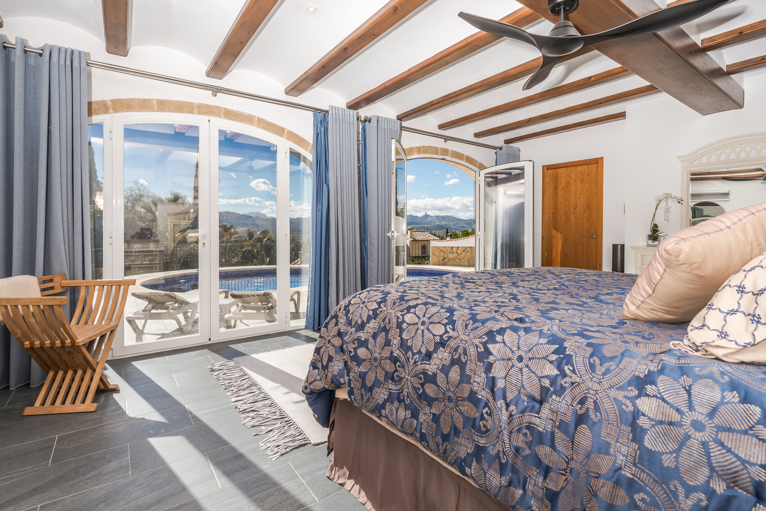 Hauptschlafzimmer mit Holzbalkendecke und Rundbogentüren aus Stein, die einen direkten Zugang zum Pool und einen weiten Ausblick bieten.