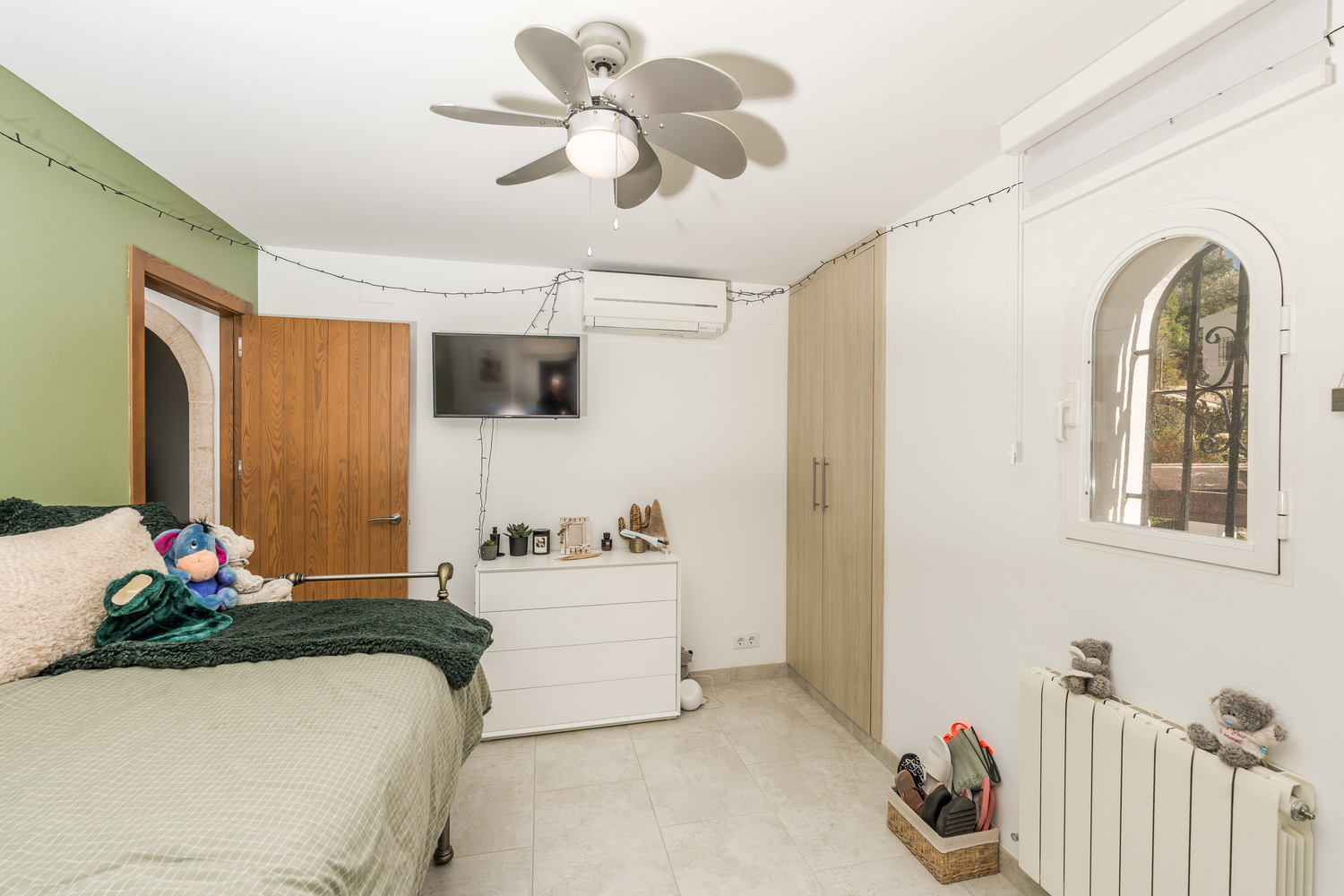 Helles Schlafzimmer mit grüner Akzentwand, Einbauschränken und Rundbogenfenster. Ausgestattet mit Deckenventilator, Klimaanlage und Zentralheizung.
