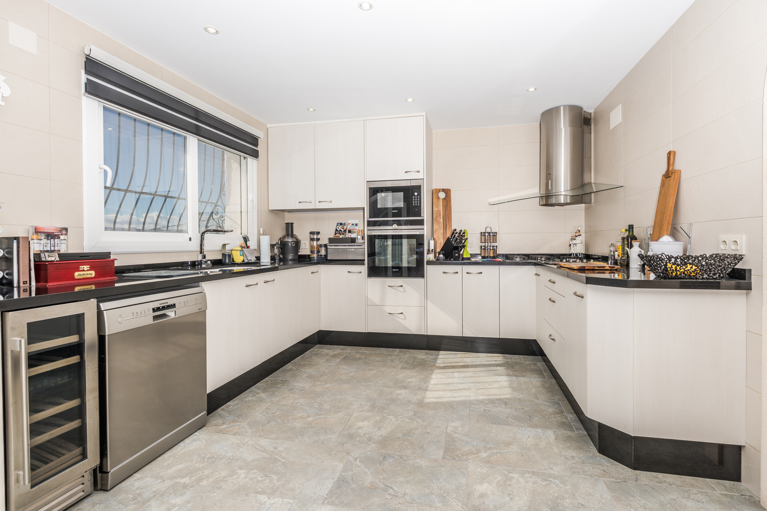 Moderne Küche mit weißen Fronten, schwarzen Arbeitsplatten und Siemens-Edelstahlgeräten, inklusive Weinkühlschrank und integriertem Backofen.