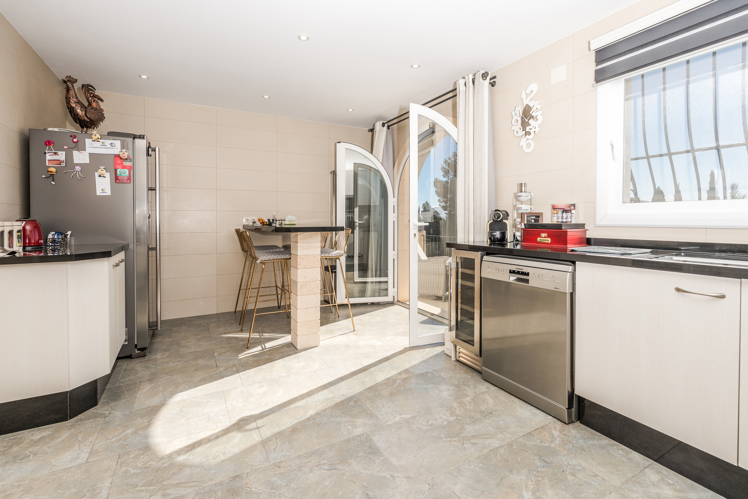 Moderne Küche mit weißen Schränken, schwarzen Granit-Arbeitsplatten und Frühstücksbar. Ausgestattet mit Edelstahlelementen und einem Rundbogen-Glaszugang zur Terrasse.