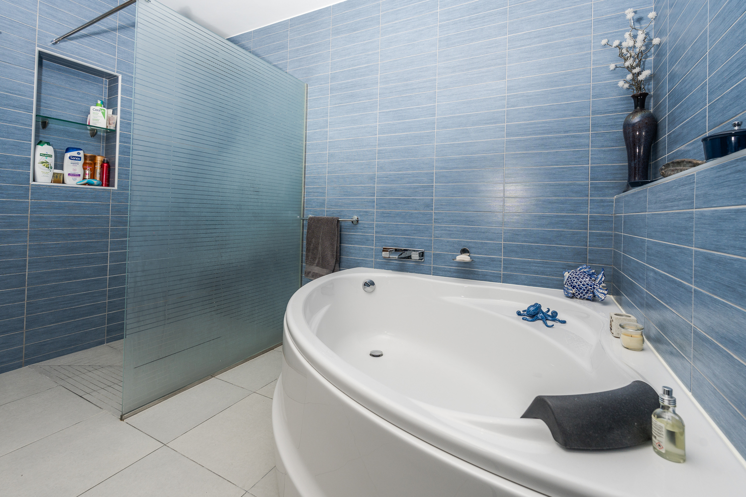 Modernes Badezimmer mit ovaler Einbaubadewanne, begehbarer Dusche mit Milchglastrennwand und horizontal strukturierten blauen Wandfliesen.