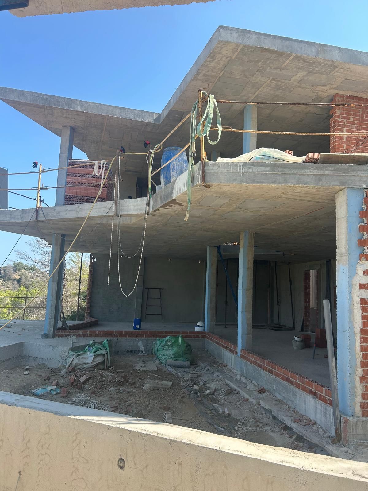Rohbauphase einer mehrstöckigen Villa in Benitachell mit Stahlbetonplatten, Pfeilern und erstem Mauerwerk unter klarem Himmel.