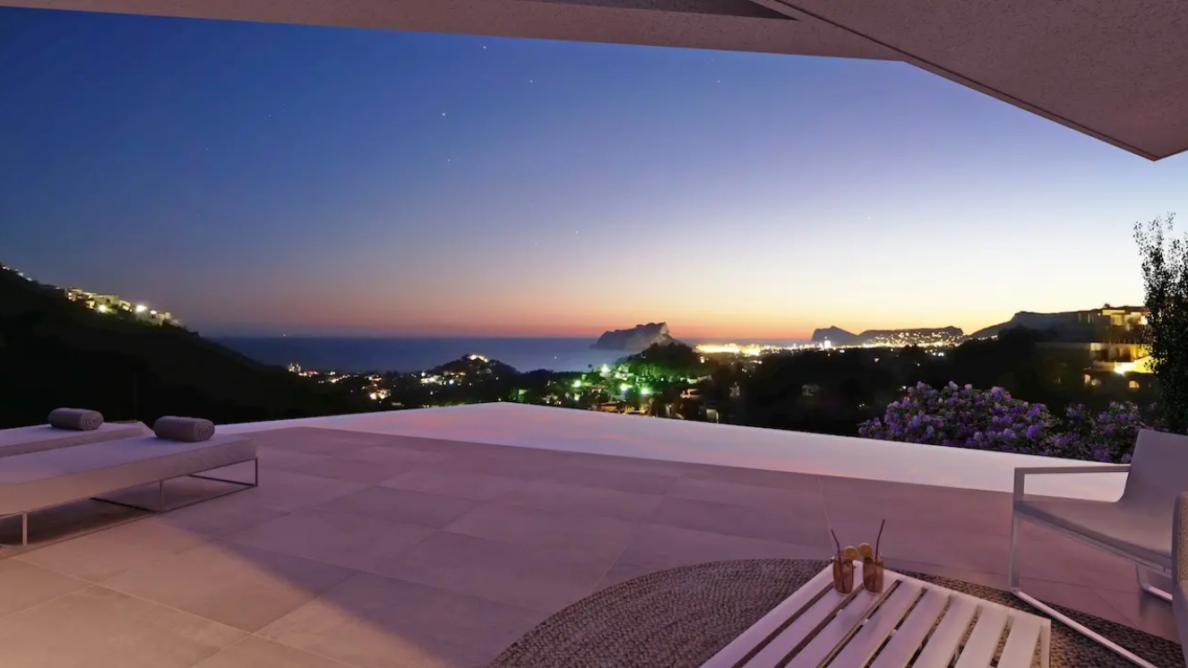 Terrasse mit Infinity-Pool und Panoramablick auf die Küste bei Dämmerung. Ausgestattet mit großformatigen Fliesen, modernen Sonnenliegen und Blick auf den Peñón de Ifach.