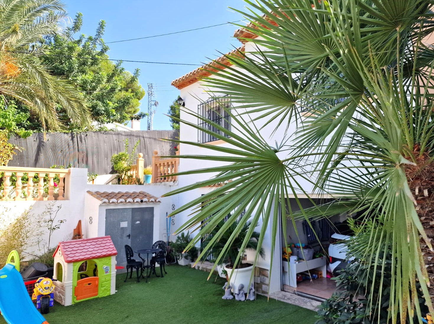 Außenansicht der unteren Ebene mit einem Kinderspielbereich auf Kunstrasen, einem separaten Lagerraum und dem offenen Zugang zur Garage.