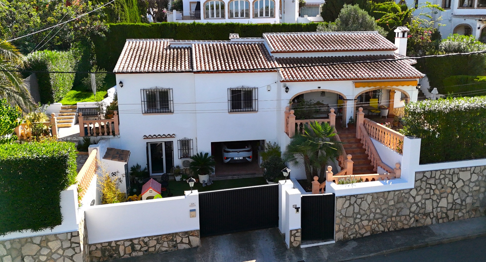 Außenansicht einer zweistöckigen mediterranen Villa mit weißer Fassade, Terrakottadach, integrierter Garage und Rundbogenterrasse mit Balustraden.