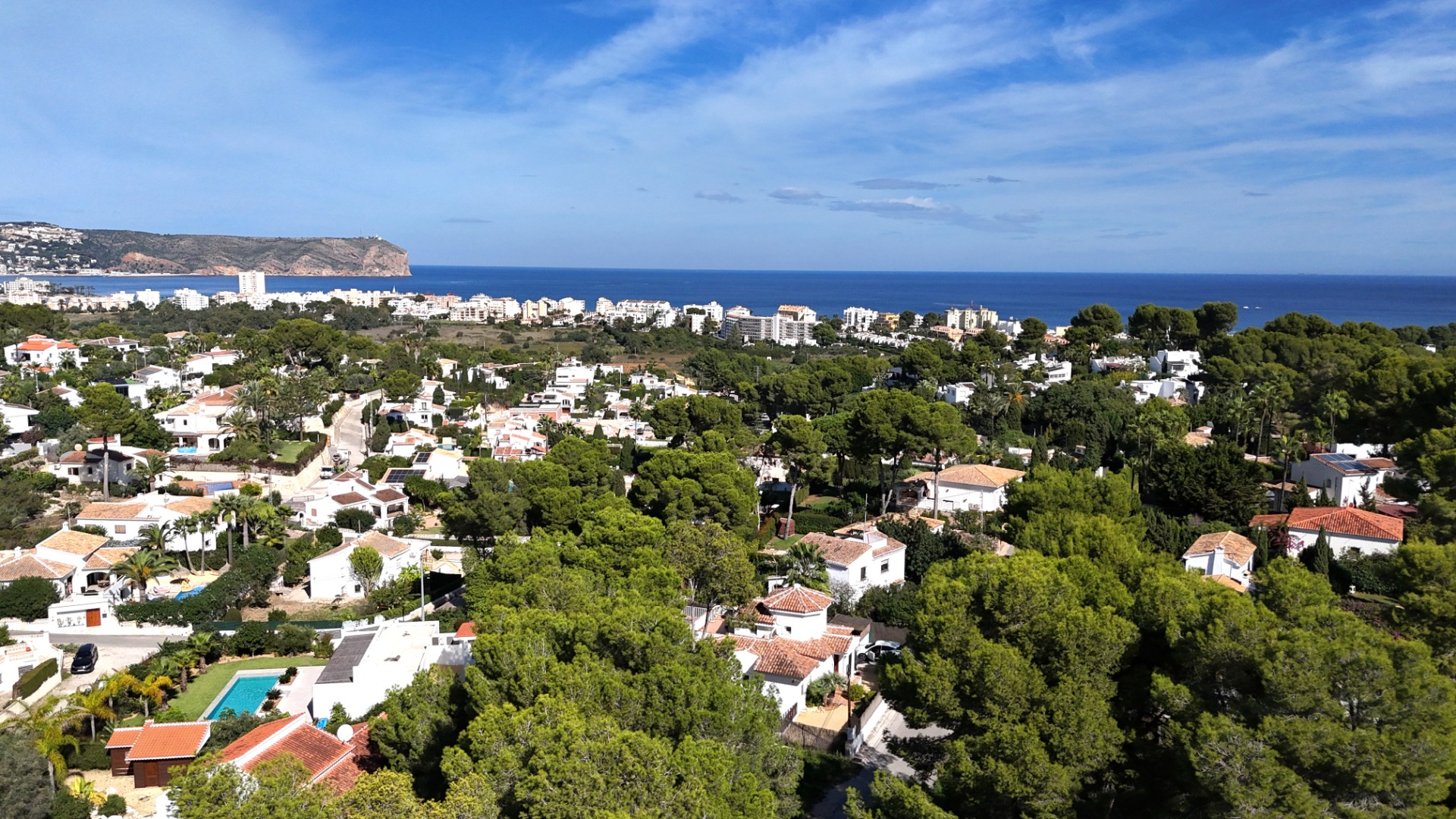Erhöhter Panoramablick auf das Wohnviertel Toscal in Jávea mit mediterranen Villen inmitten von Pinien und dem Cabo de San Antonio am Horizont.