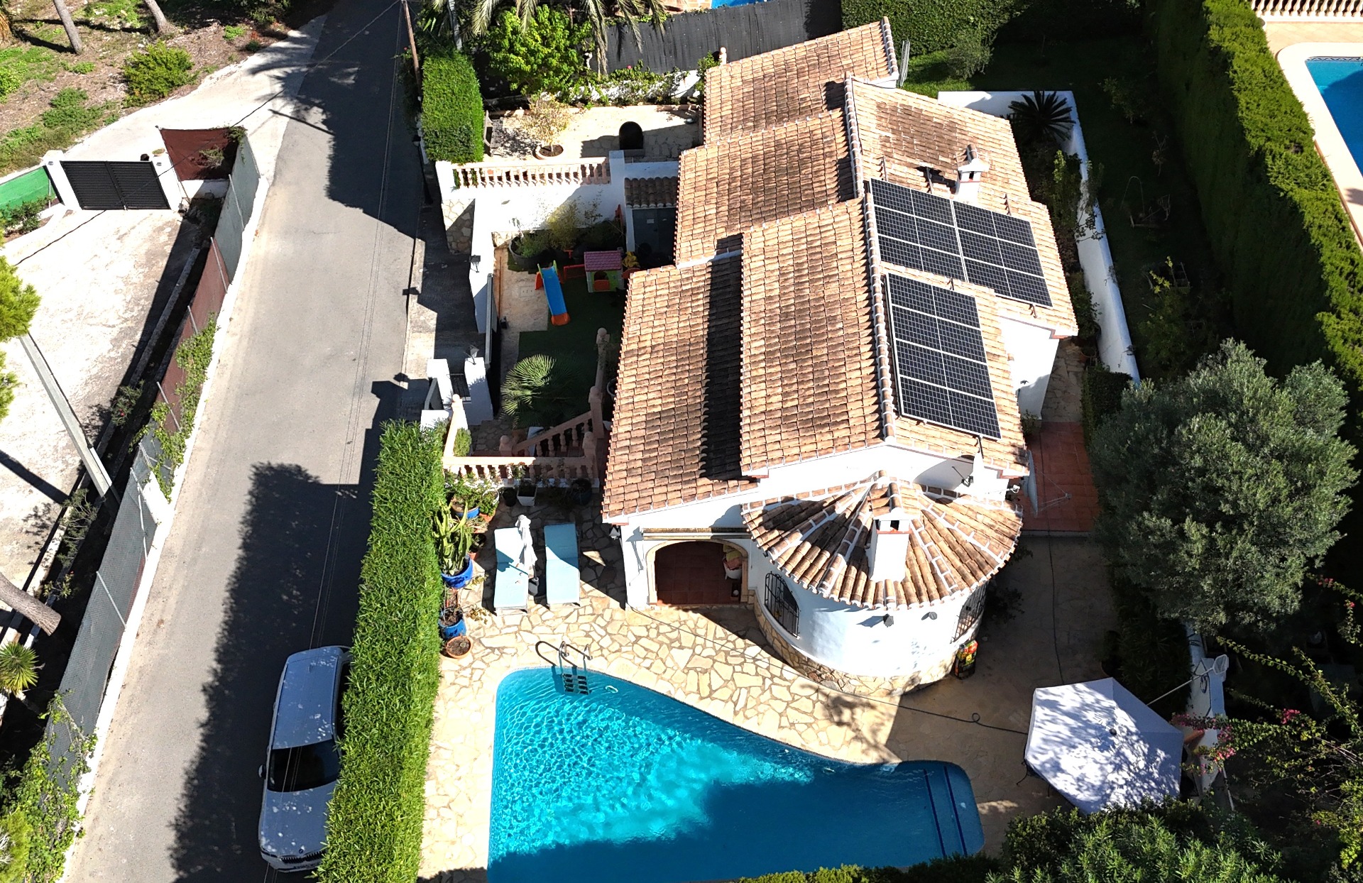 Luftaufnahme der Villa mit privatem Pool, Solaranlage auf dem Ziegeldach und einem Kinderspielplatz auf dem umzäunten Grundstück.