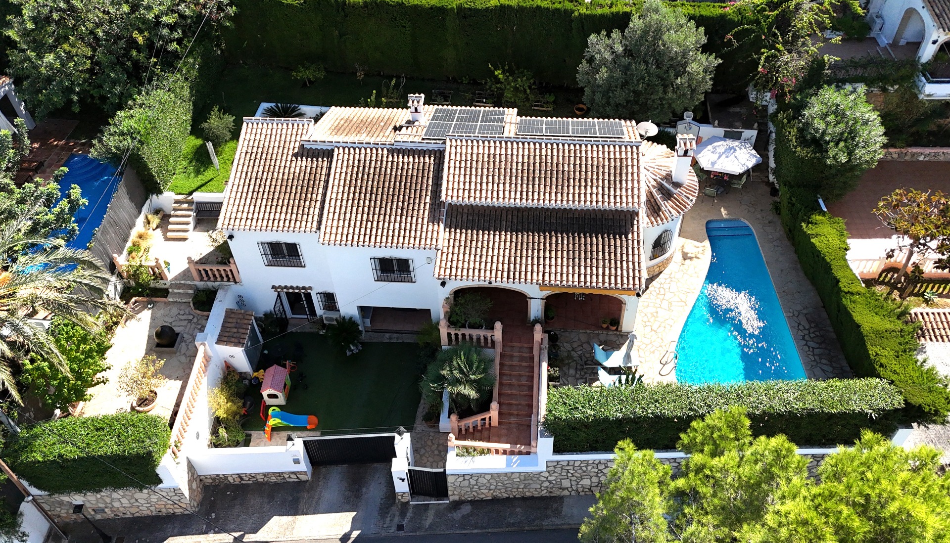 Luftaufnahme dieser Villa in Toscal mit Terrakottadach, Sonnenkollektoren, privatem Pool und Kinderspielplatz in einem gepflegten mediterranen Garten.