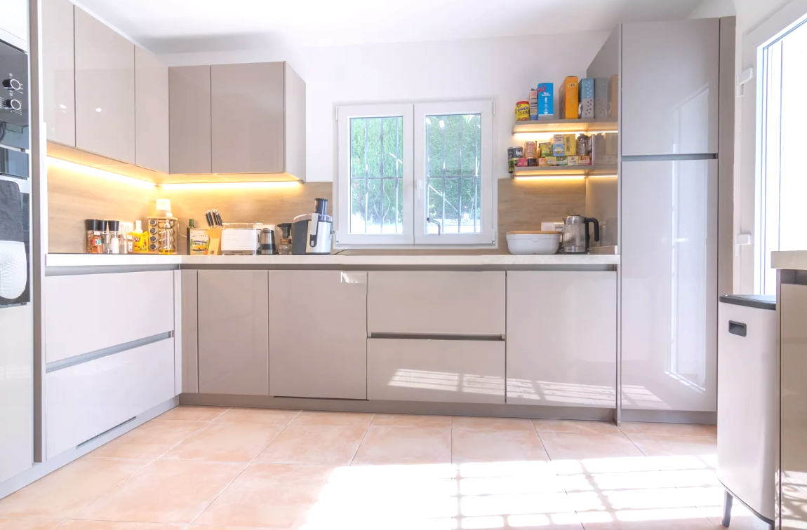 Moderne Küche mit hochglänzenden taupefarbenen Schränken, weißen Arbeitsplatten und LED-Beleuchtung. Ausgestattet mit Terrakotta-Fliesen und integrierten Geräten.