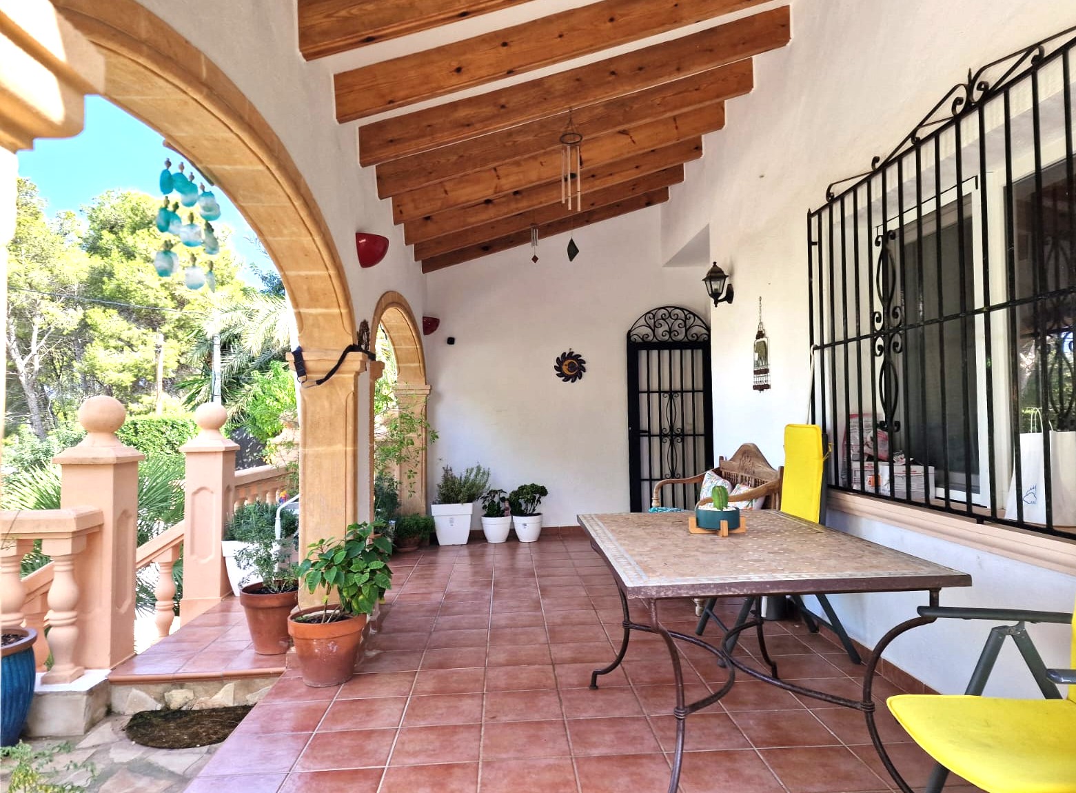 Überdachte Terrasse mit traditionellen Tosca-Steinbögen, Holzbalkendecke und Terrakottaboden. Außenbereich mit Essplatz und Blick auf das mediterrane Grün.