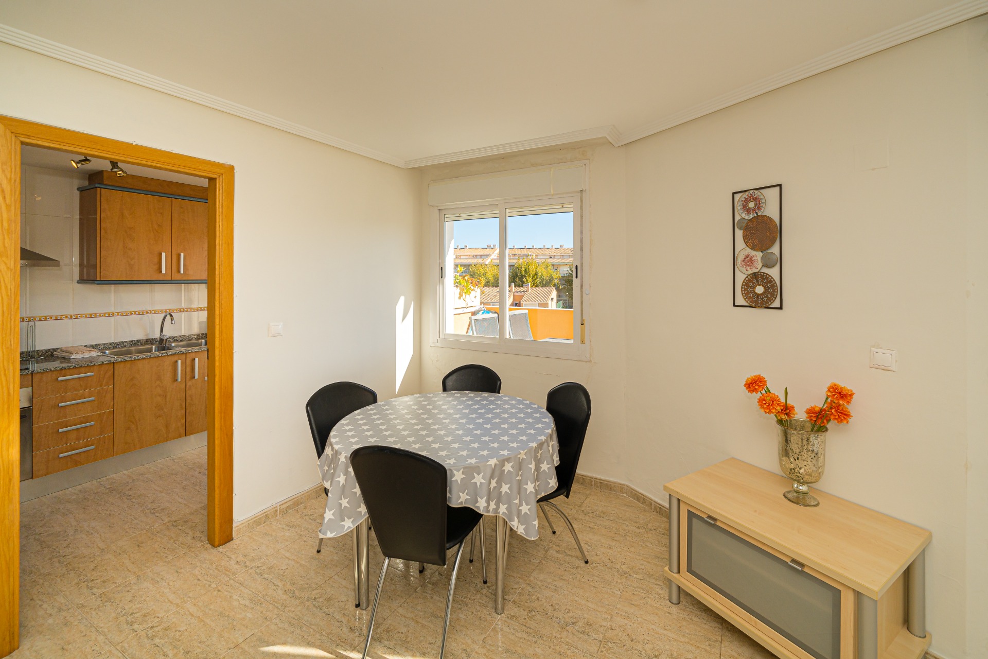 Heller Essbereich mit rundem Tisch und Fliesenboden, direkt neben der Holzküche gelegen. Das Fenster sorgt für natürliches Licht und bietet Ausblick auf die Umgebung.