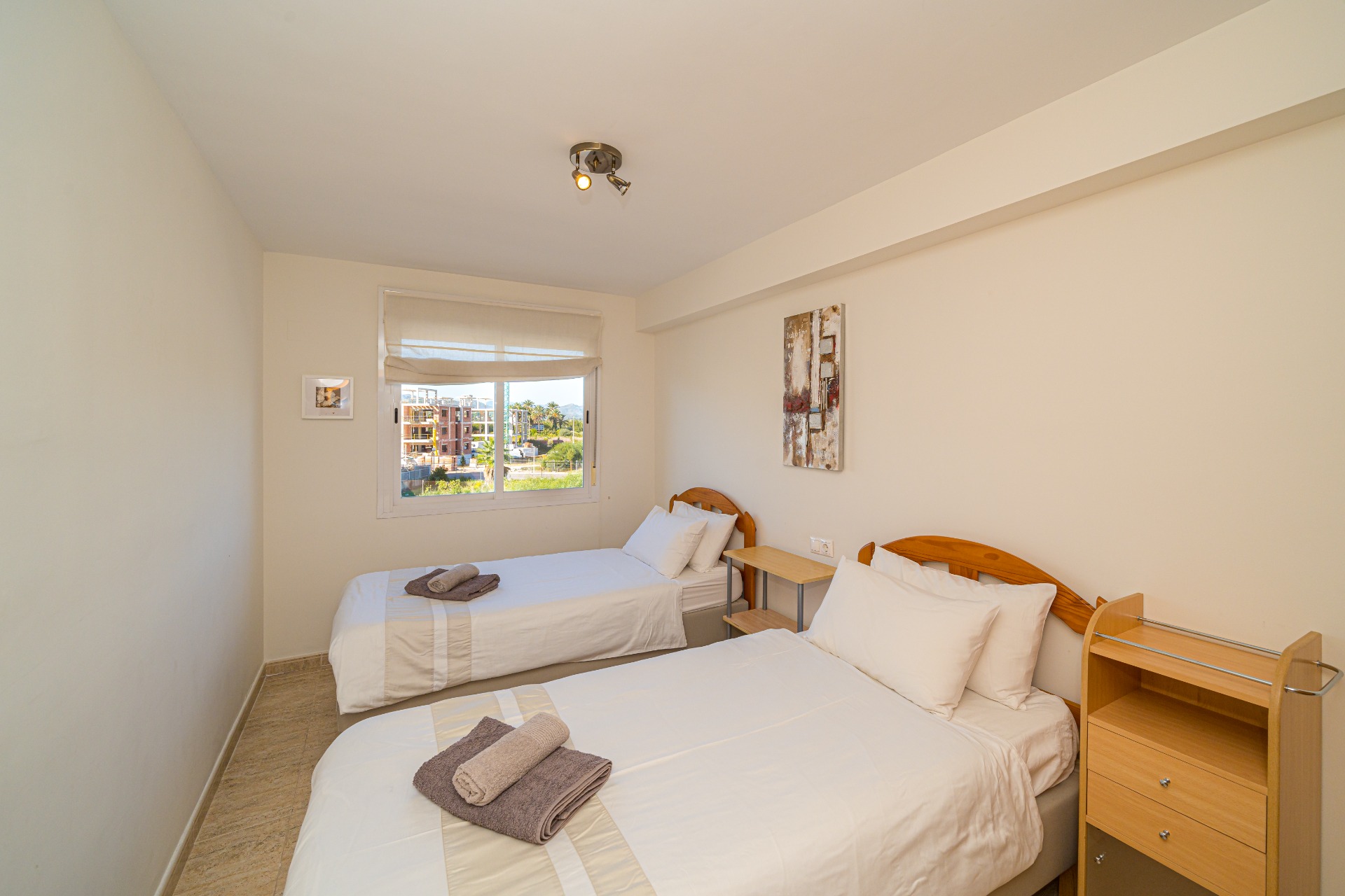 Helles Schlafzimmer mit zwei Einzelbetten, hölzernen Kopfteilen, Fliesenboden und einem Fenster, das für viel natürliches Licht und einen weiten Ausblick sorgt.