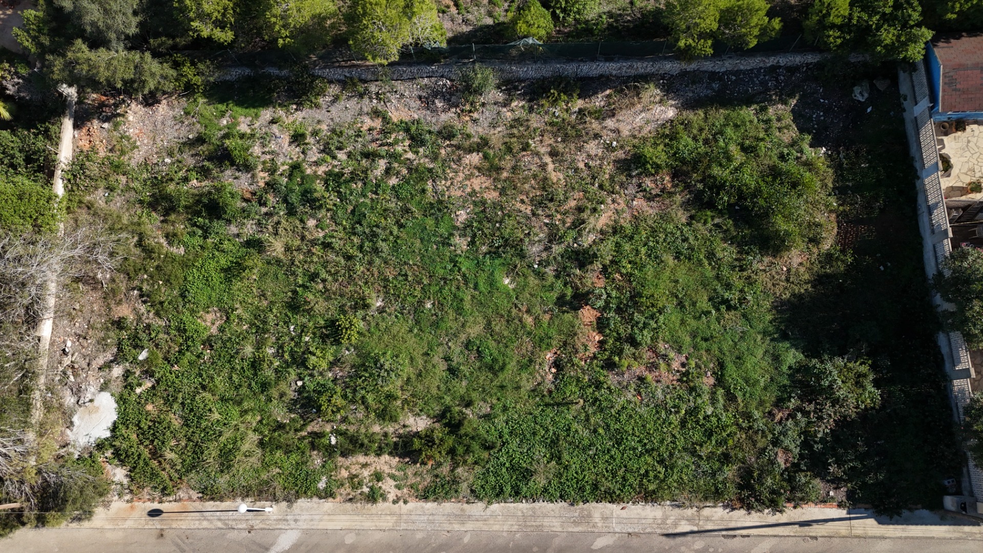 Luftaufnahme des 889 m² großen, flachen Grundstücks in Pinosol, die das rechteckige Layout, die natürliche Vegetation und den direkten Straßenzugang verdeutlicht.