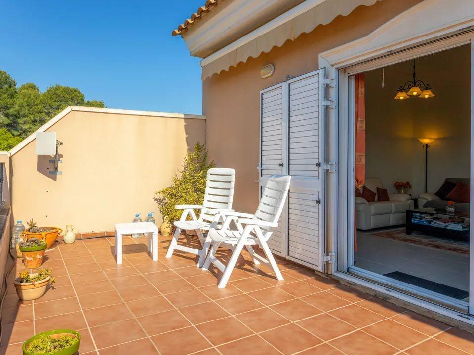 Außen-Terrasse mit Terrakotta-Fliesen, weißen Gartenstühlen und direktem Zugang zum Wohnzimmer durch Schiebetüren mit weißen Fensterläden.