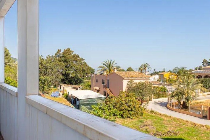 Blick vom Balkon auf das Dorf Jesús Pobre mit mediterraner Architektur, Palmen und weitem Ausblick über die umliegende Landschaft unter blauem Himmel.
