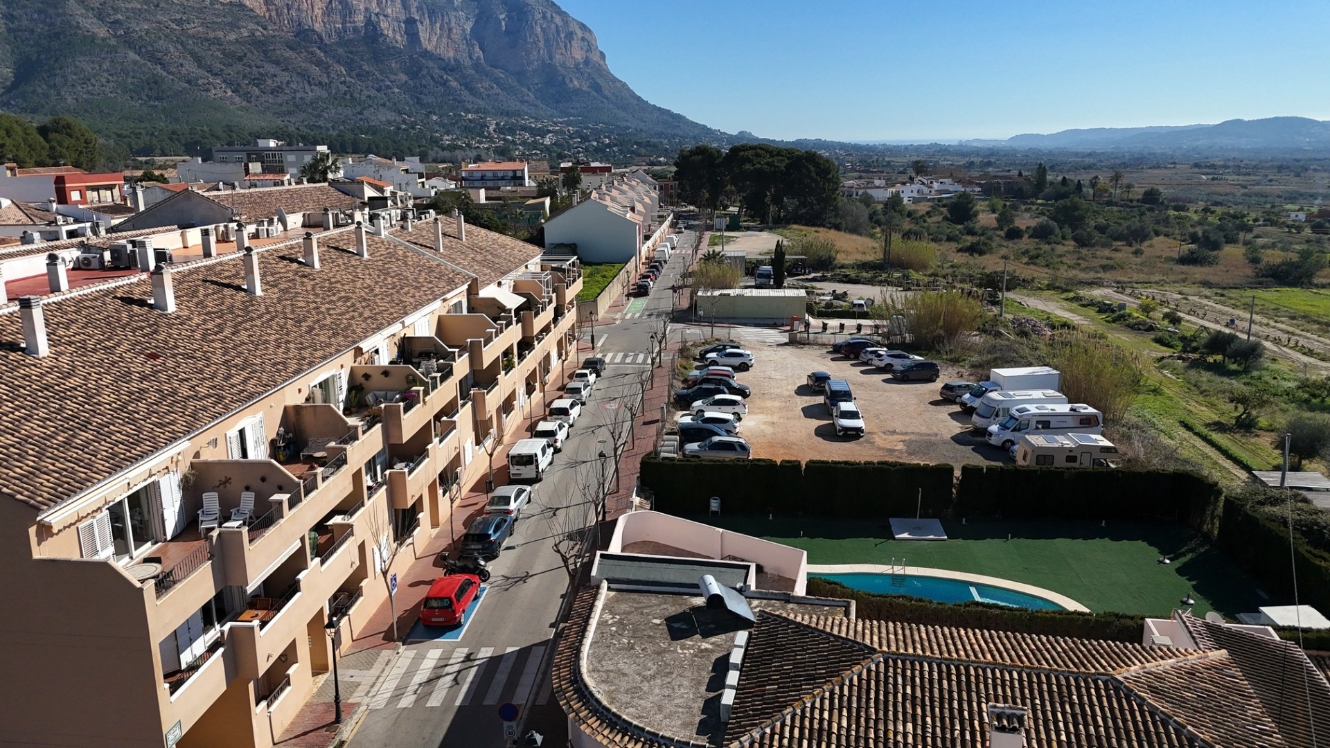 Erhöhte Ansicht der Wohnanlage mit Gemeinschaftspool, Parkplätzen und Panoramablick auf das Montgó-Massiv und die umliegende Landschaft.