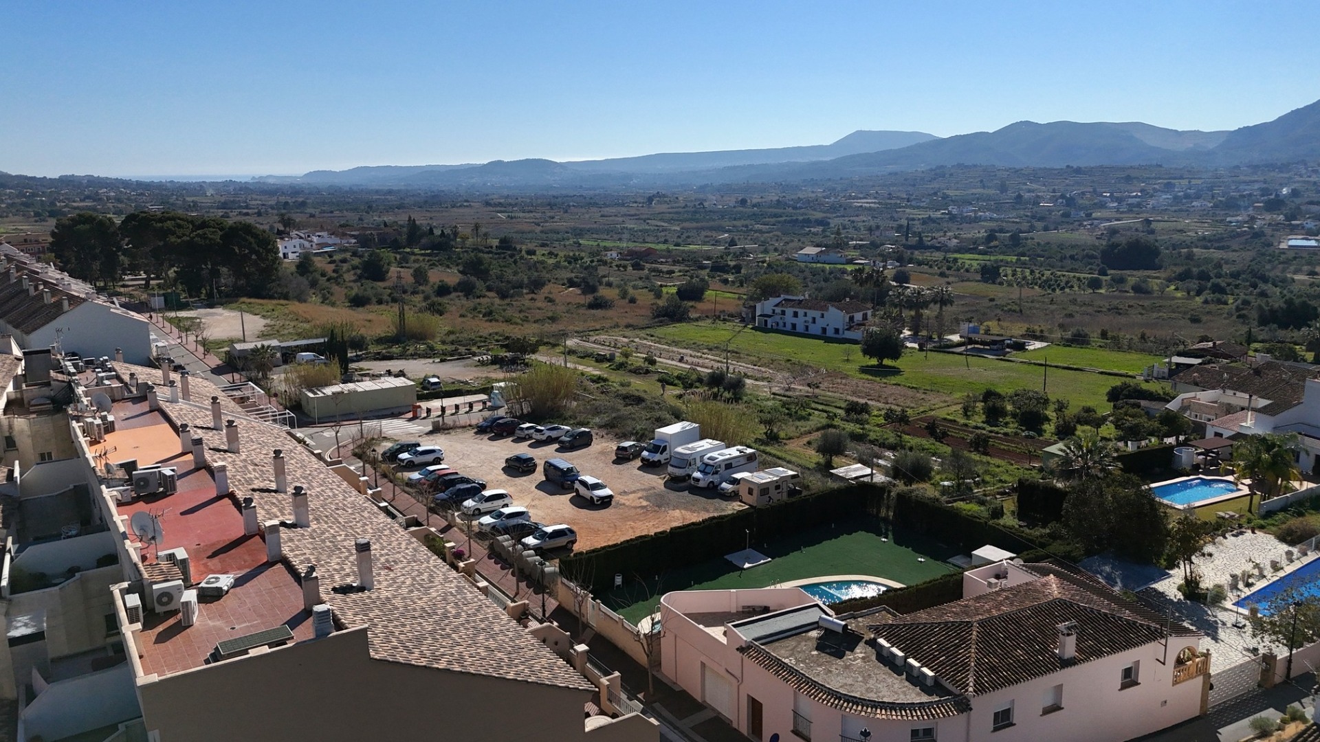 Erhöhter Blick vom Penthouse auf den Gemeinschaftspool, die Parkflächen und die weite Landschaft bis hin zu den fernen Bergen.