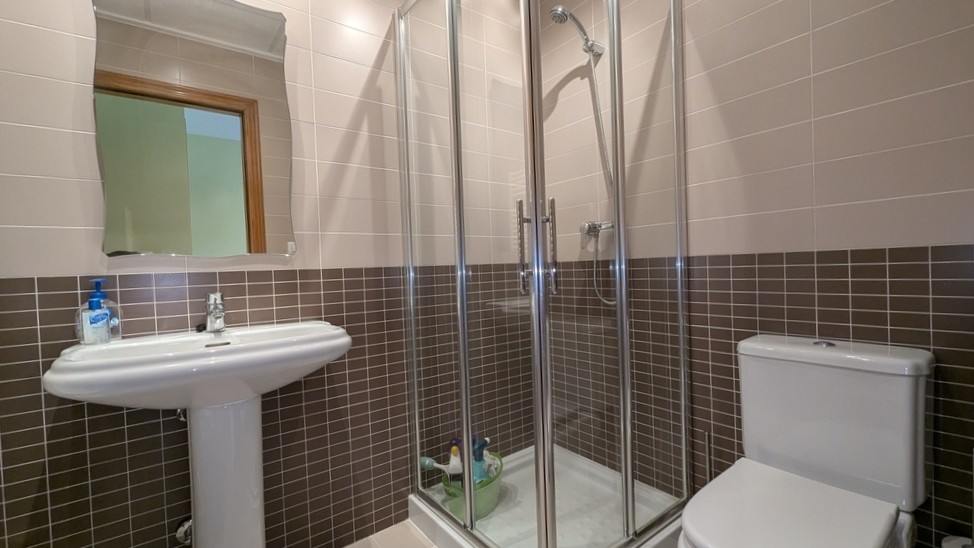 Funktionales Badezimmer mit Eckglasdusche, Standwaschbecken und zweifarbiger Wandverfliesung in Braun und Beige.