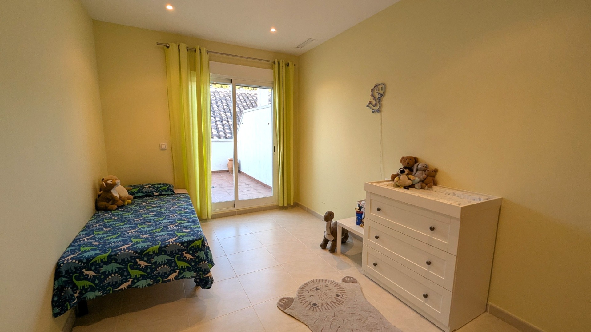 Helles Schlafzimmer mit Fliesenboden, lindgrünen Vorhängen und Glasschiebetür, die direkten Zugang zu einer privaten Außenterrasse bietet.