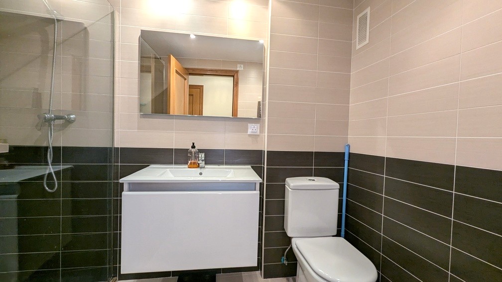 Modernes Badezimmer mit zweifarbigen Wandfliesen, weißem Hängewaschtisch, rechteckigem Spiegel und Dusche mit Glastrennwand.