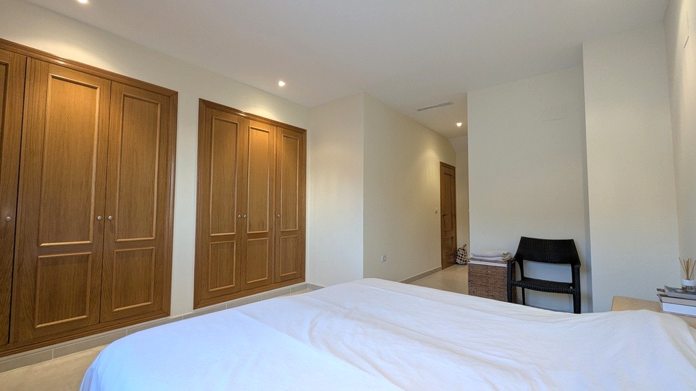 Schlafzimmer mit großzügigen Einbauschränken aus Holz, Deckeneinbaustrahlern und hellen Fliesenböden.