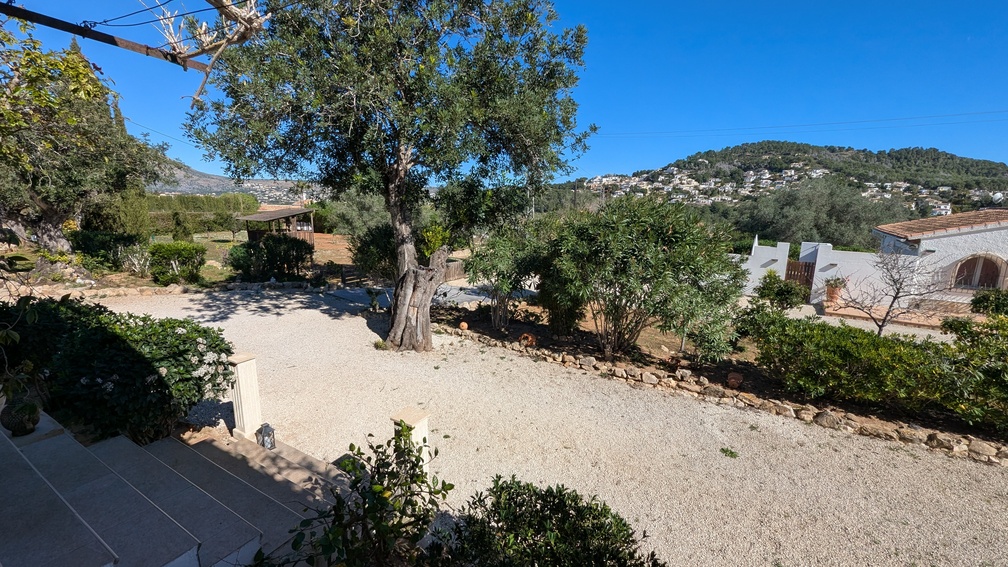 Erhöhte Ansicht der Kiesauffahrt und der mediterranen Gärten mit alten Olivenbäumen und Blick auf die umliegenden Hügel und Wohngebiete von Jávea.