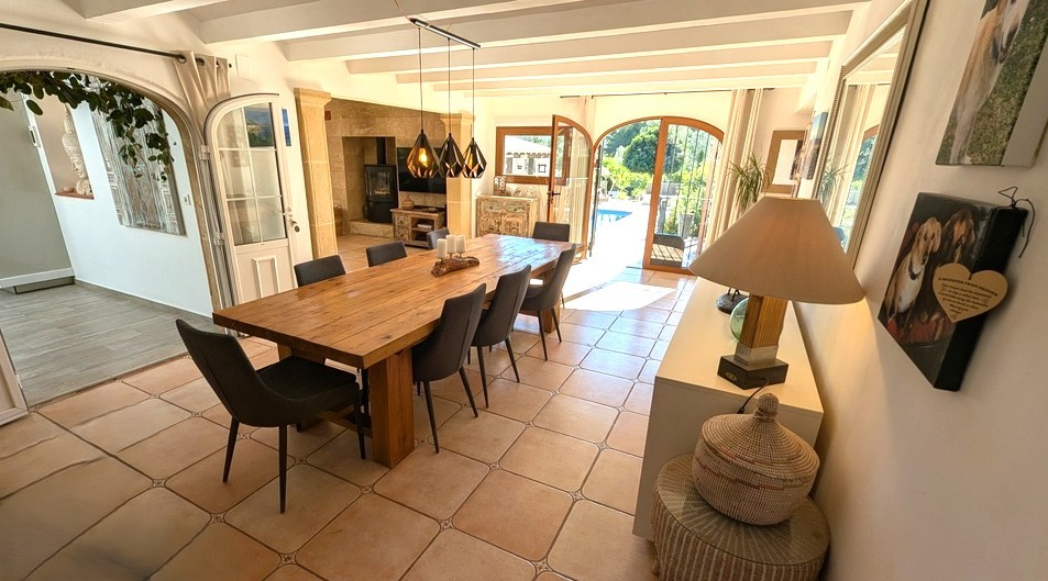 Heller Essbereich mit Massivholztisch, weißen Deckenbalken und Terrakottafliesen. Rundbogige Glastüren führen direkt zur Terrasse und bieten Blick auf den Poolbereich.