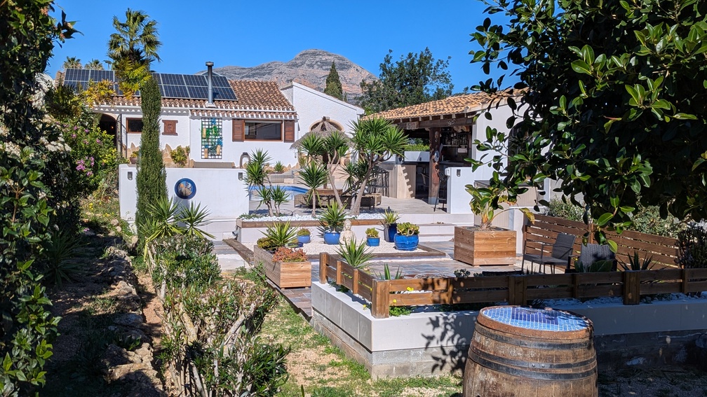 Mediterraner Garten mit terrassierten Ebenen, Außenküche und Villa mit Solarmodulen, vor der markanten Kulisse des Berges Montgó.