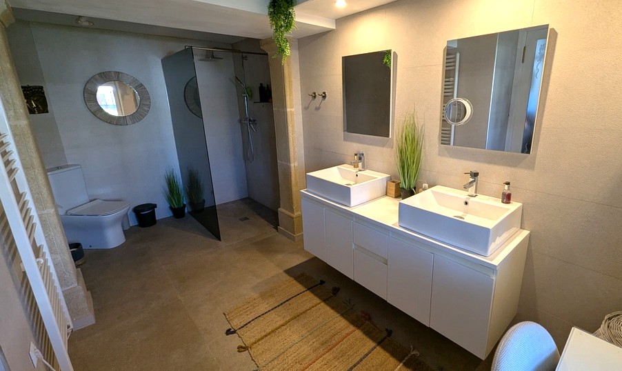 Modernes Badezimmer mit Doppelwaschtisch, begehbarer Dusche mit getönter Glaswand und hochwertigen Steinfliesen in neutralen Erdtönen.