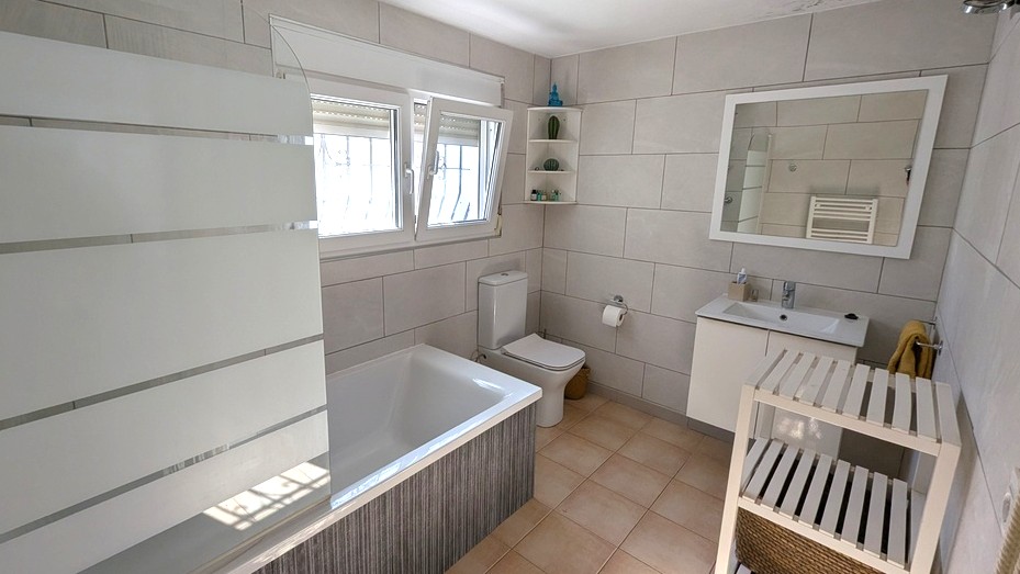 Modernes Badezimmer mit Einbaubadewanne, satinierter Glastrennwand, weißem Waschtisch und großformatigen Wandfliesen in neutralen Tönen.