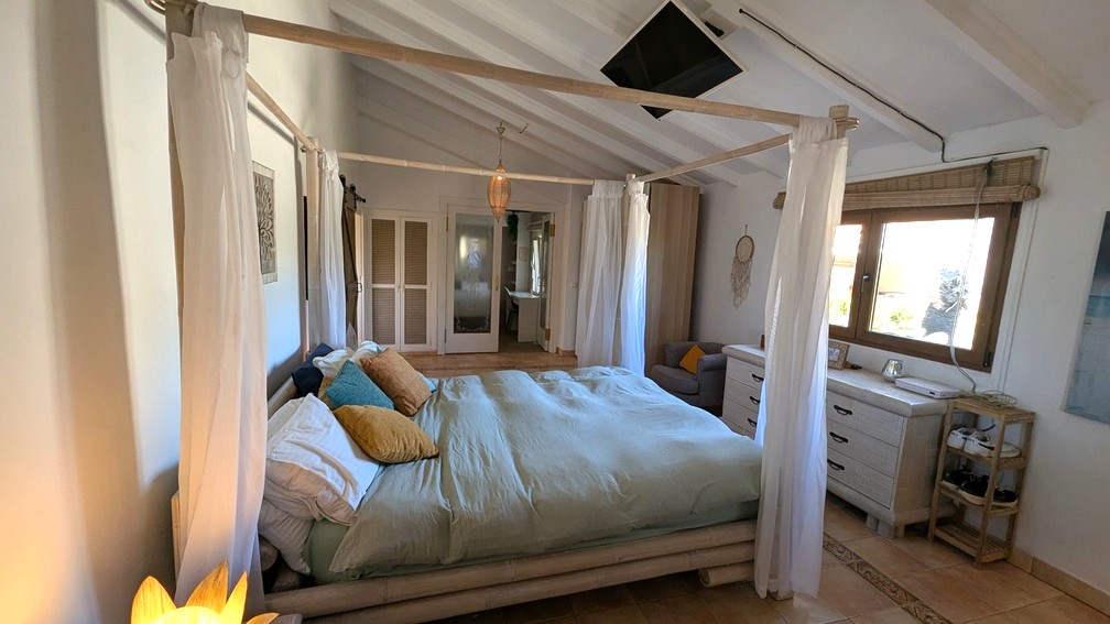 Schlafzimmer mit Bambus-Himmelbett, weißer Balkendecke und Terrakottafliesen. Ausgestattet mit Decken-TV und Zugang zu praktischen Einbauschränken.