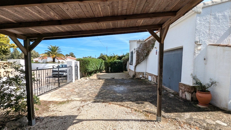 Blick vom hölzernen Carport auf die gepflasterte Einfahrt, das Garagentor und das schmiedeeiserne Tor zum Grundstück.