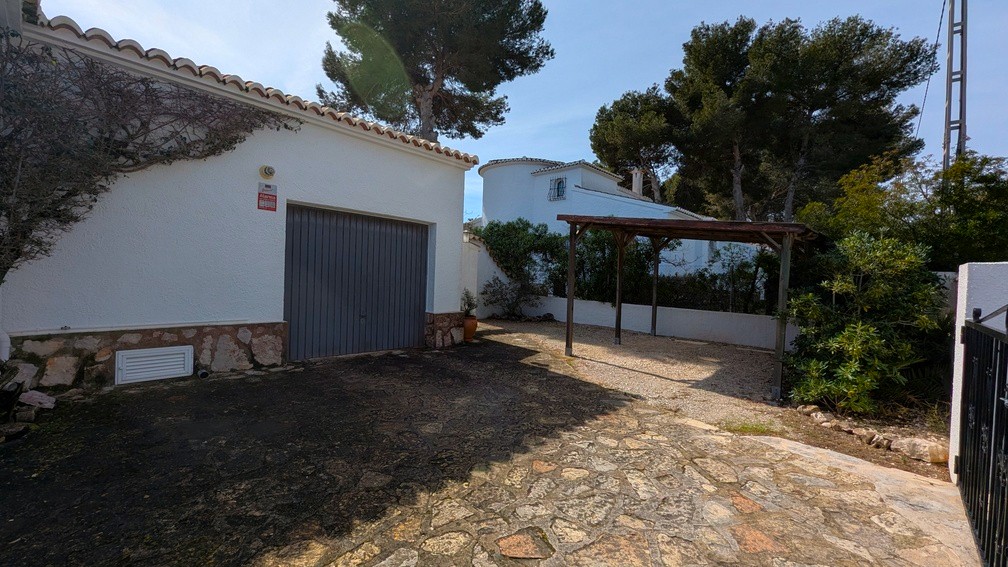 Garagenbereich mit grauem Tor und Holz-Carport, ergänzt durch eine Natursteinzufahrt und weiße Fassade mit Steinsockel.