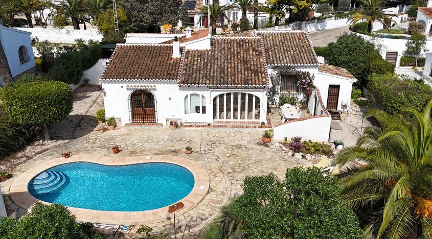 Luftaufnahme der Villa mit nierenförmigem Pool, Natursteinterrasse und mediterraner Architektur mit Terrakotta-Ziegeldächern und weißen Außenwänden.