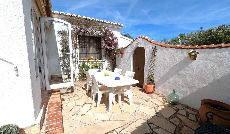 Private Außenterrasse mit Natursteinpflaster, weißer Essgruppe und traditioneller mediterraner Architektur mit Rundbogentüren und Terrakotta-Dachziegeln.