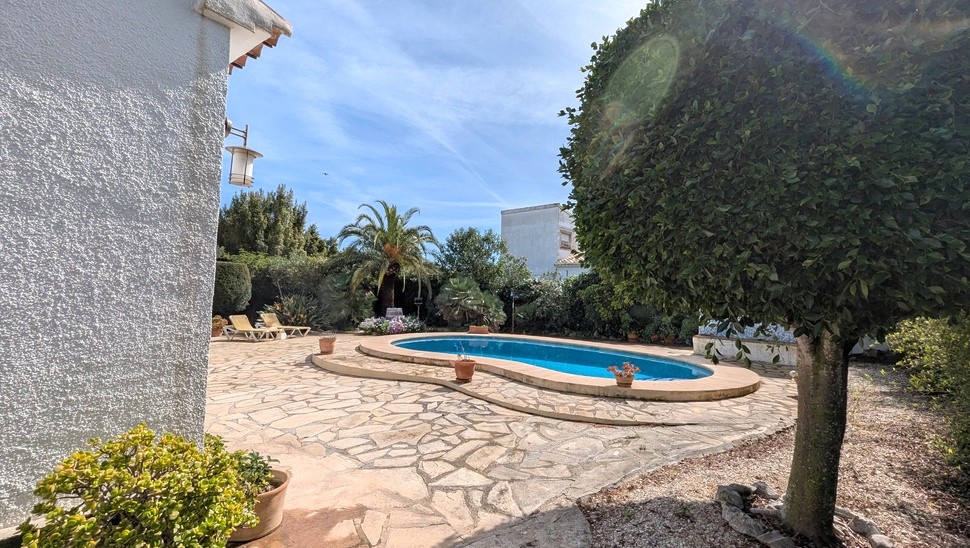 Privater nierenförmiger Pool, umgeben von Natursteinpflaster und einem eingewachsenen mediterranen Garten mit Palmen und Liegeflächen.