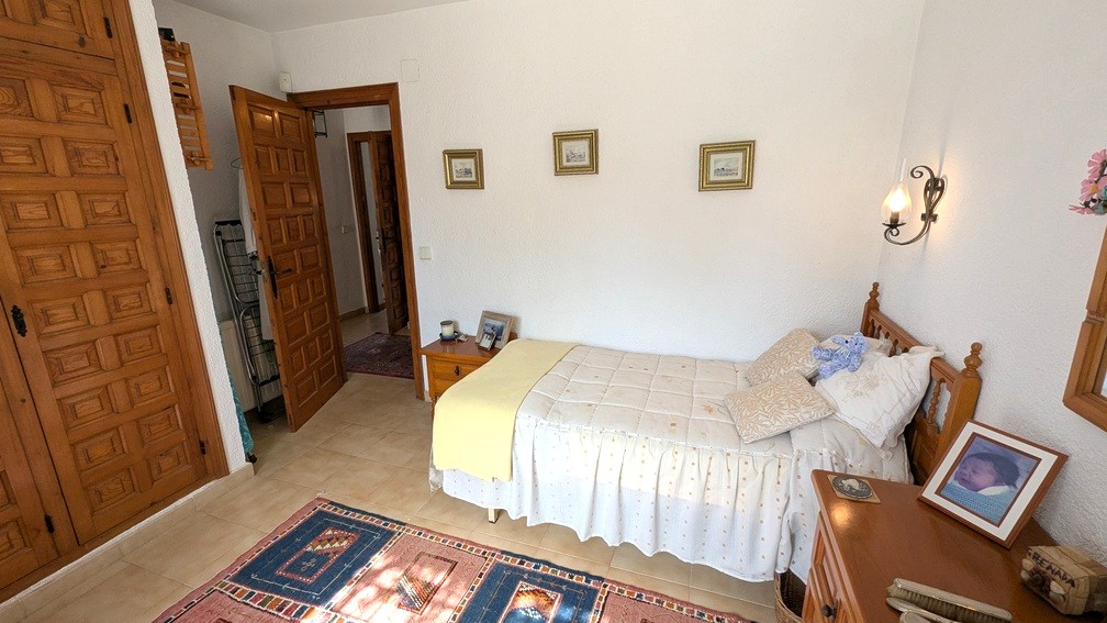 Schlafzimmer mit traditionellen Einbauschränken aus geschnitztem Holz, Fliesenboden und Einzelbett. Rustikale Holztüren und weiße Strukturwände prägen den Raum.