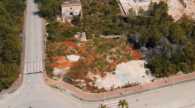 Luftaufnahme des 1.000 m² großen Eckgrundstücks in Villas del Vent mit roter Erde, umliegenden Pinien und vollständig erschlossener Straßeninfrastruktur.