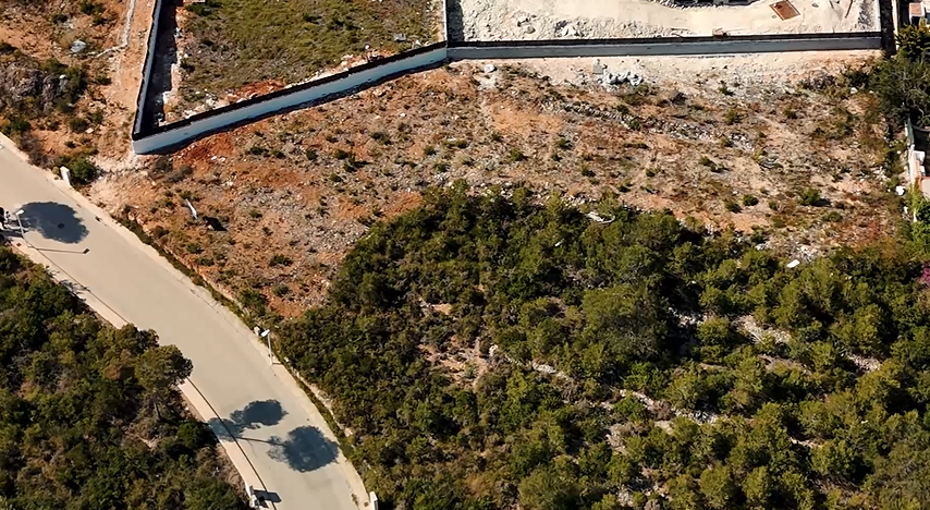Luftaufnahme des 1.528 m² großen Grundstücks in Lomas del Rey mit Blick auf das ausgehobene Gelände, die Stützmauer und die asphaltierte Zufahrtsstraße.