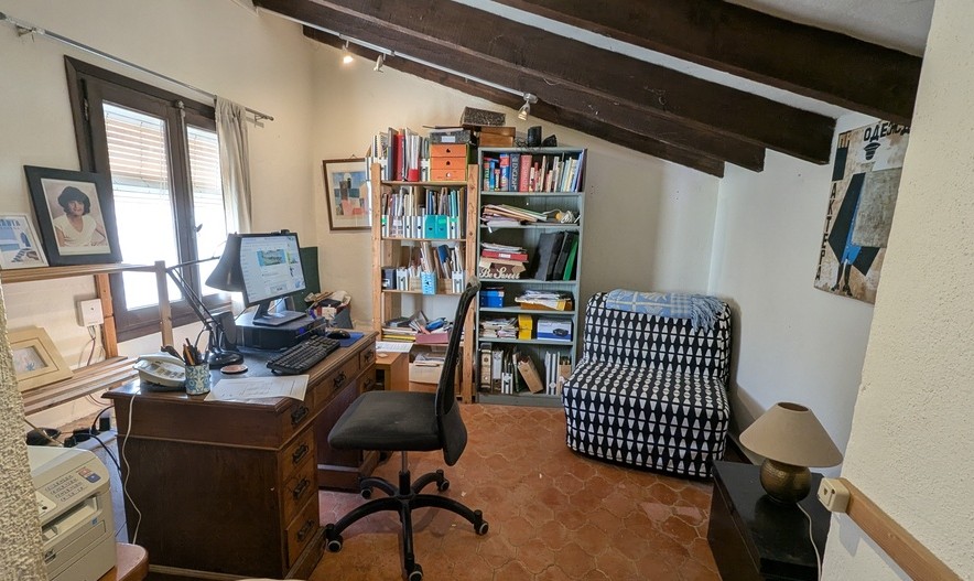 Arbeitszimmer mit traditionellem Terrakottaboden, dunklen Sichtholzbalken an der Dachschräge und einem klassischen Holzschreibtisch mit Tageslicht.