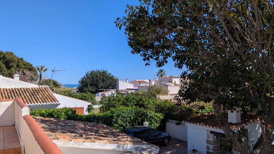 Blick von der oberen Terrasse über traditionelle Ziegeldächer und dichte Vegetation bis hin zum fernen Mittelmeer am Horizont.