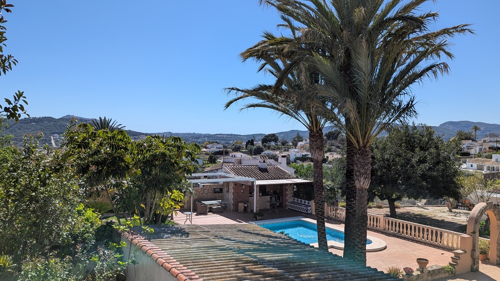 Erhöhter Blick auf den privaten Pool und die Terrasse mit traditioneller Außenküche, Palmen und weitem Ausblick auf die Hügellandschaft von Javea.