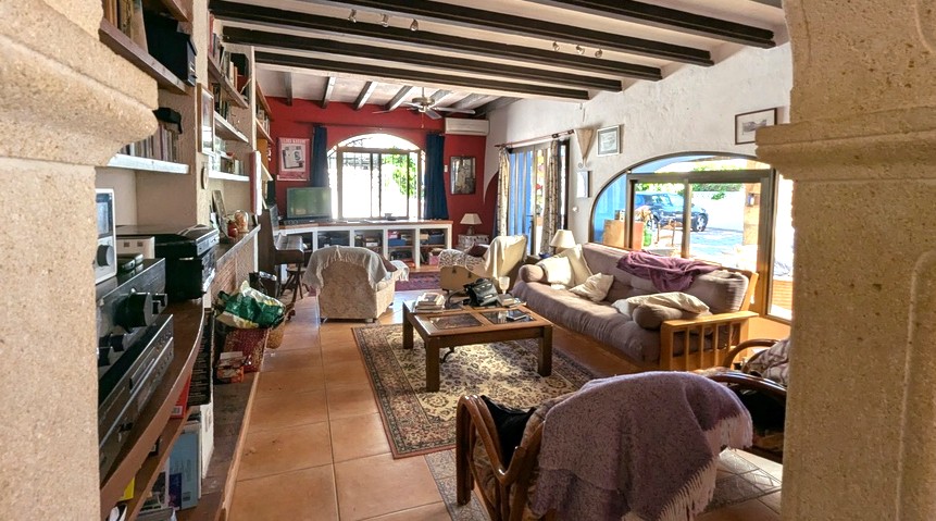 Großzügiges Wohnzimmer mit dunklen Holzbalkendecken, Tosca-Steinbögen, Terrakottaböden und großen Fenstern, die für viel Tageslicht sorgen.