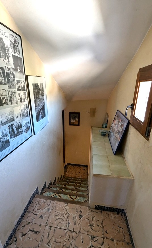Innenliegende Treppe mit traditionellen gemusterten Bodenfliesen und dekorativen Mosaik-Setzstufen. Ein Holzfenster und gerahmte Kunstwerke zieren den Aufgang.