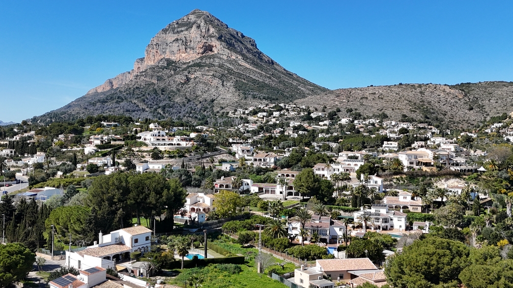 Panoramablick auf den Berg Montgó über die Wohnlandschaft von Javea, mit traditionellen weißen Villen und üppiger mediterraner Vegetation unter blauem Himmel.