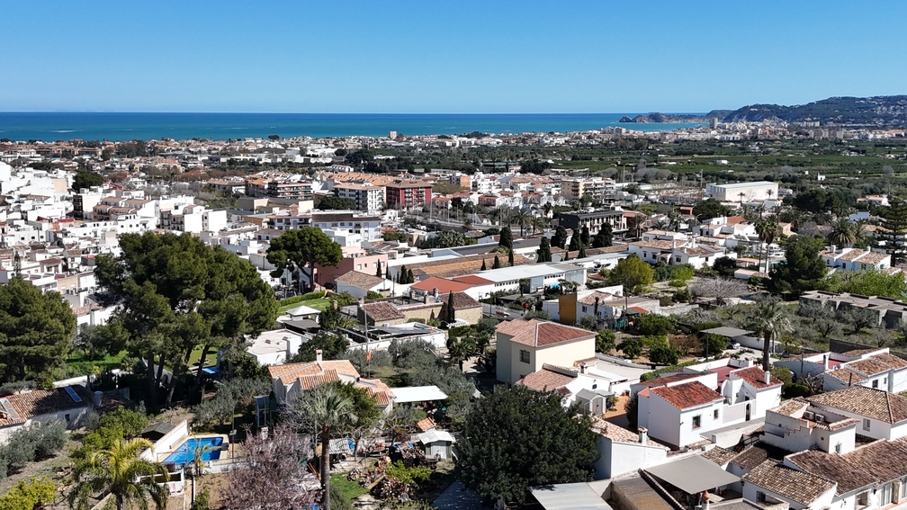 Panoramablick von der Terrasse über die Dächer von Javea Pueblo bis hin zum Mittelmeer und der fernen Küstenlinie unter blauem Himmel.
