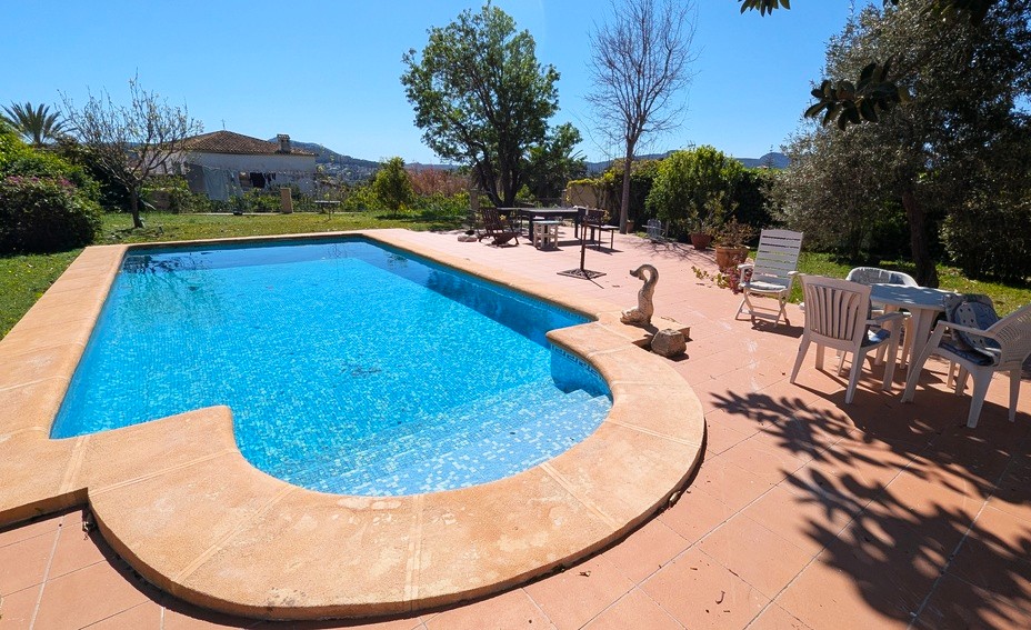 Privater Pool mit blauen Mosaikfliesen, umgeben von einer großzügigen Terrasse aus Terrakotta-Steinen und einem gepflegten Garten mit weitem Bergblick.