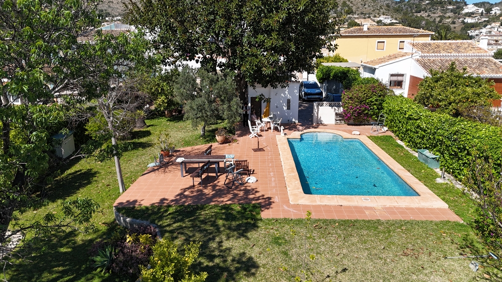 Privater Pool mit einer Terrasse aus Terrakottafliesen und Rasenfläche. Alter Baumbestand und Hecken bieten Sichtschutz für den Essbereich und den Garten.
